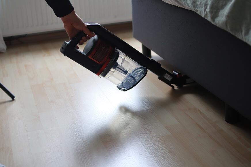 Man sieht den Shark Anti Hair Wrap Flexoloxy bei der Reinigung unter Möbeln.